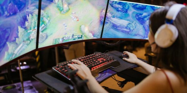 a woman playing League of Legends on three-monitor PC setup