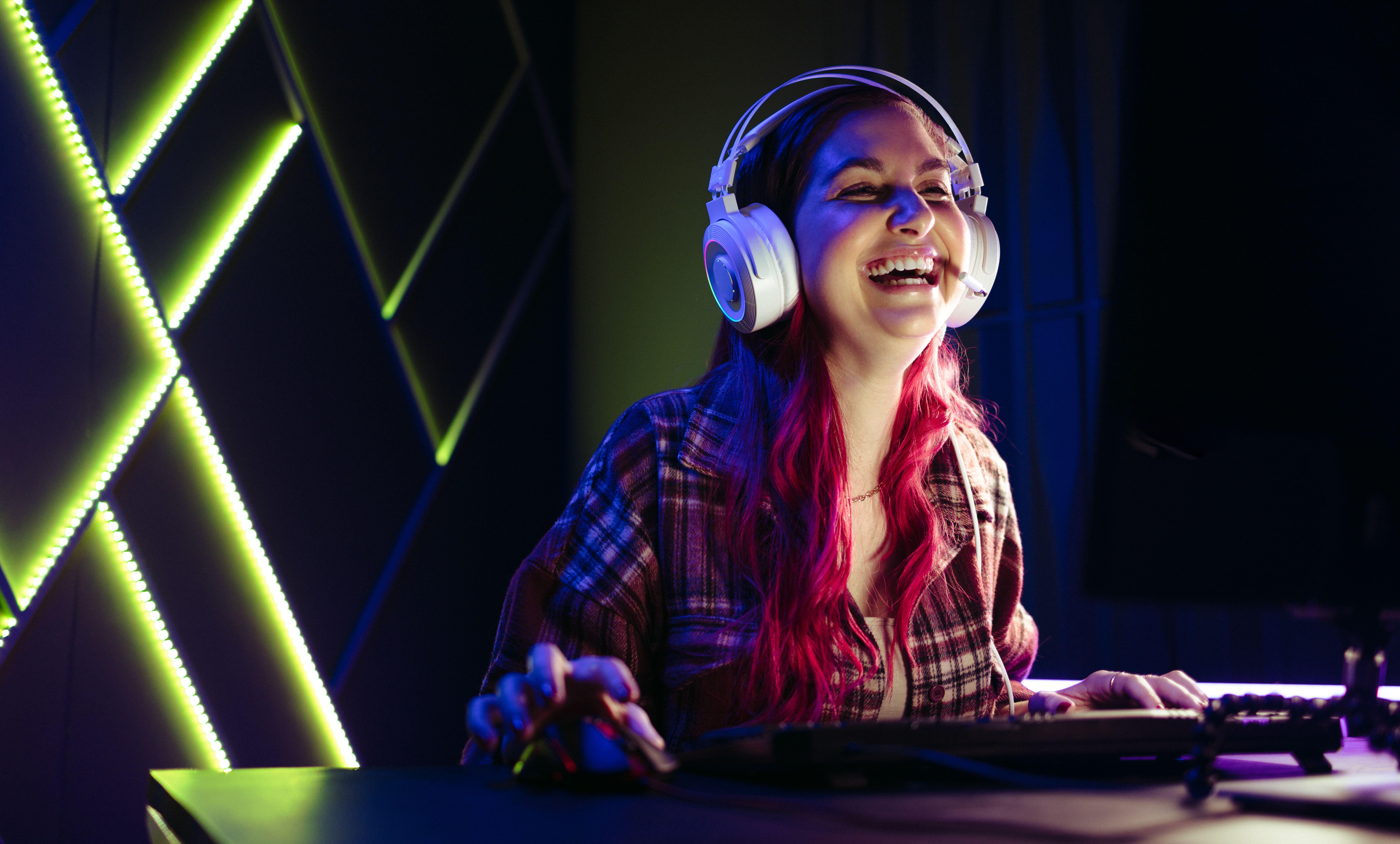 a woman laughing while playing Clair Obscur: Expedition 33 on her PC inside an LED lit room